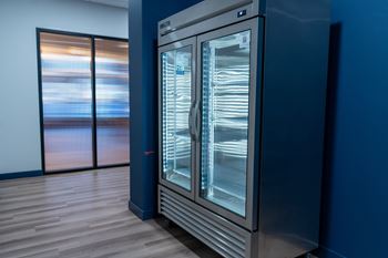 A large, modern refrigerator with its door open, standing in a room with wooden flooring and a blue wall.